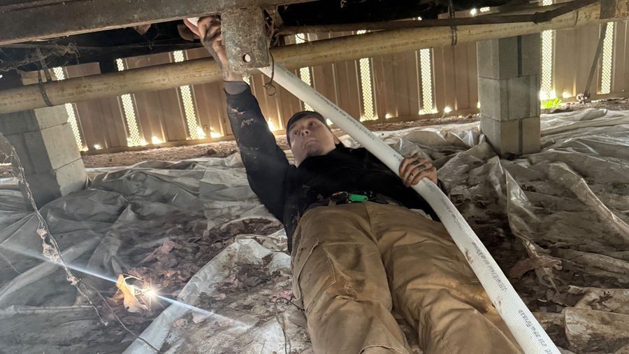 VAC technician working on ductwork in a crawl space beneath a home.